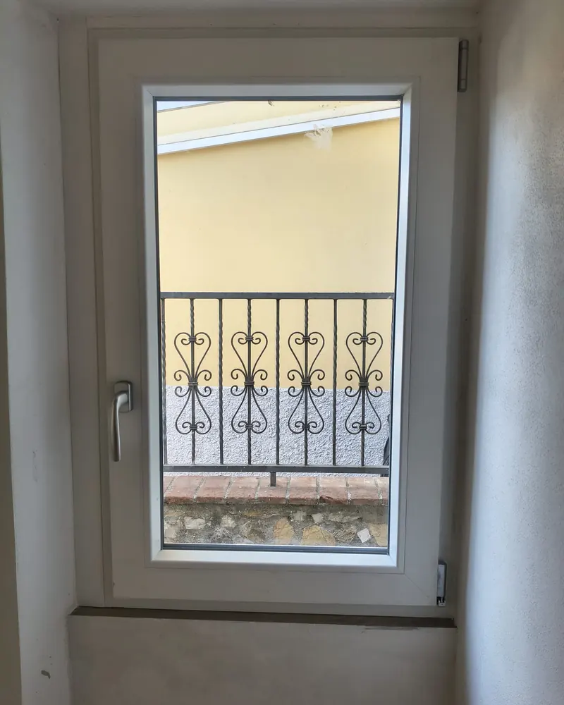 Finestra a un’anta in PVC bianco che si affaccia su una ringhiera in ferro battuto