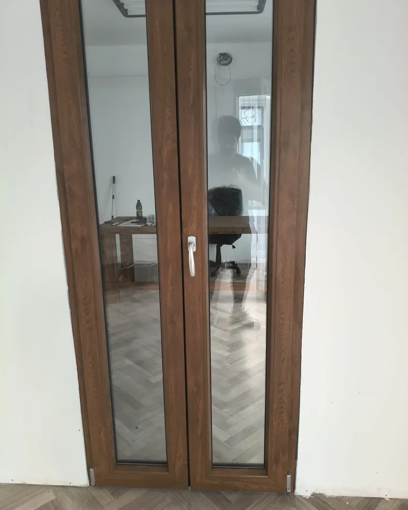 Portafinestra a due ante strette in PVC effetto legno noce, vista da dentro casa su un pavimento a spina